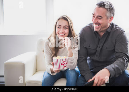 Portrait of a young man and daughter watching TV while eating popcorn on the sofa Stock Photo