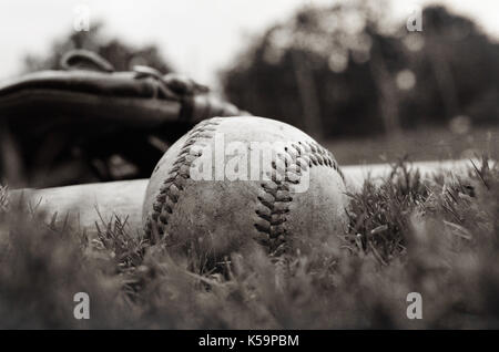 Old vintage baseball on grass after game with glove and bat in background. Stock Photo