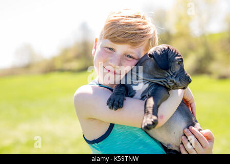 Cute, young boy in the garden holding a boxer dog Stock Photo