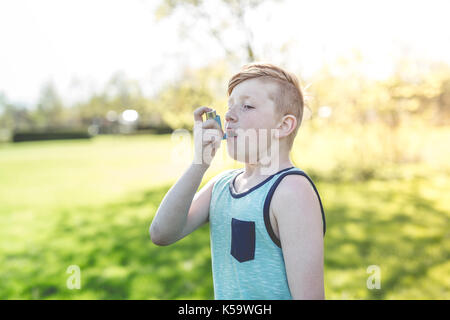 Boy using an asthma inhaler in the park Stock Photo