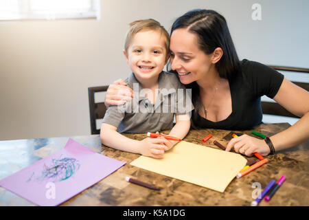 Child drawing with his mom, sitting at table in kitchen at home