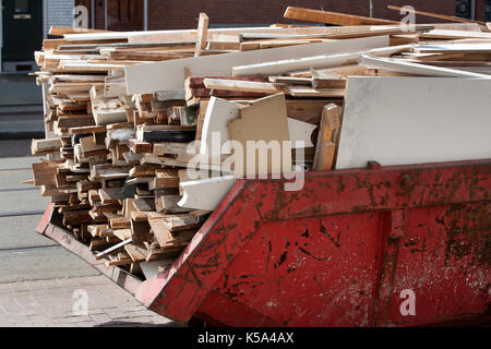 Rust red skip loaded with a pile of old, dirty wood because of home improvement or renovation Stock Photo