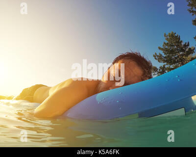 Man floating on inflatable mattress in swimming pool in summer sunset in privacy of backyard private house poolside Stock Photo