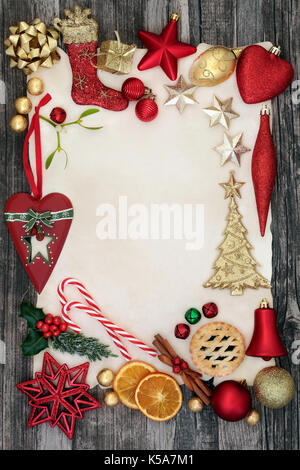 Christmas background border with bauble decorations with holly, mistletoe, fir, cinnamon spice, dried orange fruit and mince pie on distressed wood. Stock Photo