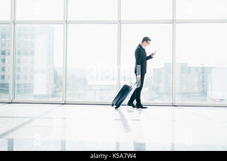 Businessman at international airport moving to terminal gate for airplane travel trip with phone in hand Stock Photo