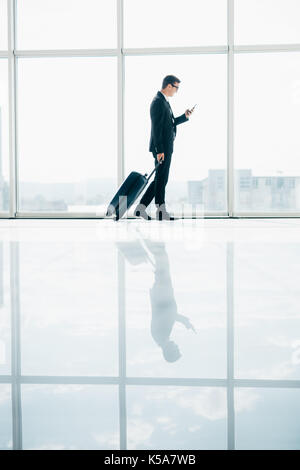 Businessman at international airport moving to terminal gate for airplane travel trip with phone in hand Stock Photo