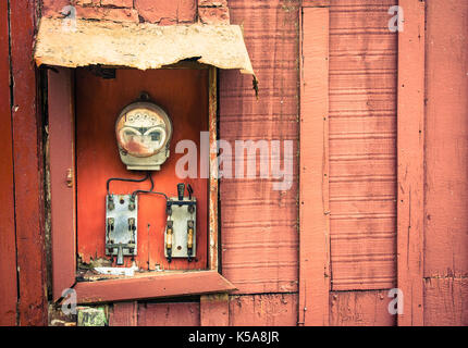 Old vintage and rusted analog electricity meter counter used for measurements in kWh of electricity usage with two switches on a red cracked and peeli Stock Photo