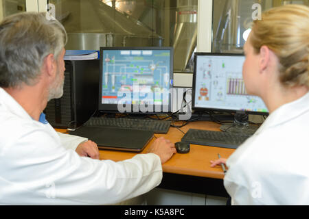 Technicians using computers overlooking vats Stock Photo