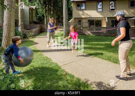 Young girl playing skipping rope game with adults. Stock Photo