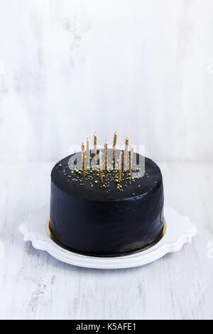 Black birthday cake with golden candles on white background Stock Photo