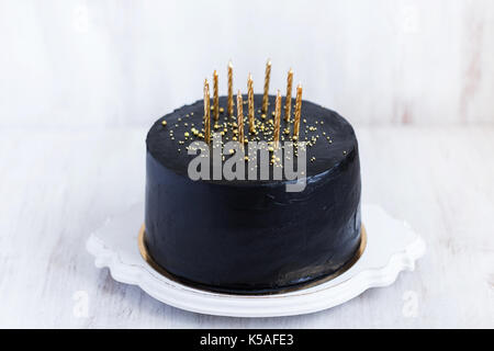 Black birthday cake with golden candles on white background Stock Photo