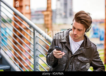Handsome young man standing outdoors in urban environment on metal stairs, using cell phone Stock Photo