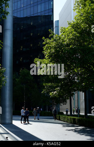Pedestrians walking past large modern buildings in London in the Sun with shadows cast across floor Stock Photo