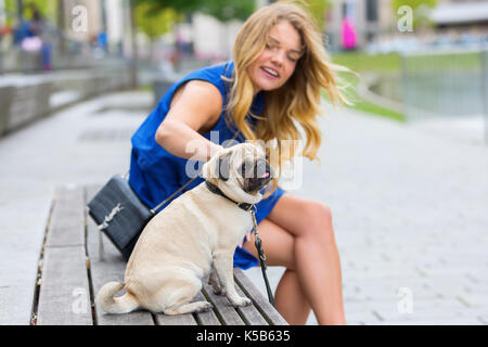 pretty young woman sits with a cute pug on a bench in the city Stock Photo