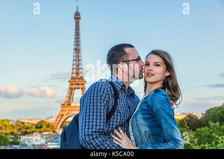 Tourist couple in Paris is kissing in the evening with Eiffel Tower in background. Stock Photo