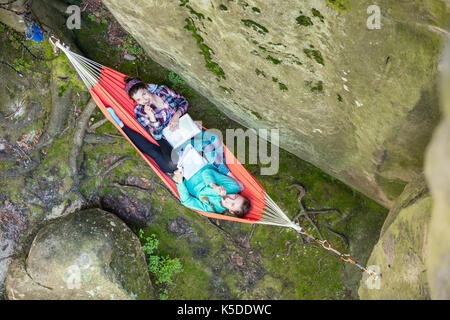 Young women reading books and eating chocolate while relaxing in hammock near cliff, view from above Stock Photo
