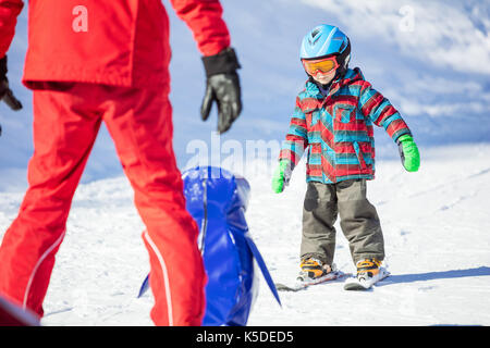 Young skier sliding down towards towards toy penguin and ski instructor. Ski lesson in alpine school. Stock Photo