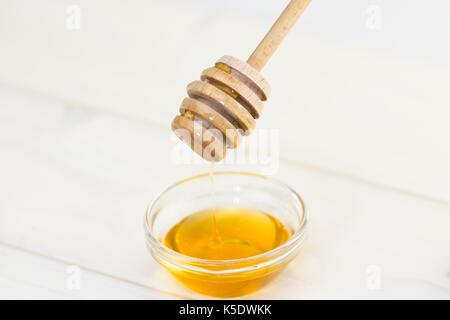 Honey dipper transferring honey and dripping into small glass bowl.Selective focus on the dipper Stock Photo