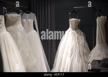 Selection of white wedding dresses or ball gowns on display hanging on rails with selective focus to one illuminated by a highlight Stock Photo