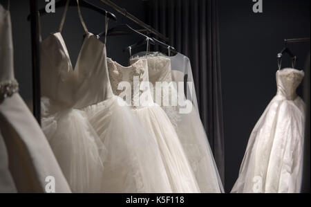 Selection of white wedding dresses or ball gowns on display hanging on rails with selective focus to one illuminated by a highlight Stock Photo