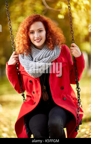 Red haired curly woman on a swing in park in autumn Stock Photo