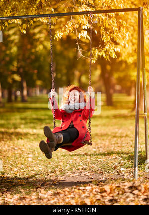 Young happy redhead woman on swing in park in autumn Stock Photo