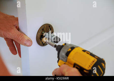 Installation of door lock using a screwdriver to. Carpenter at lock installation with electric drill into wood door. Installation lock. Carpenter inst Stock Photo