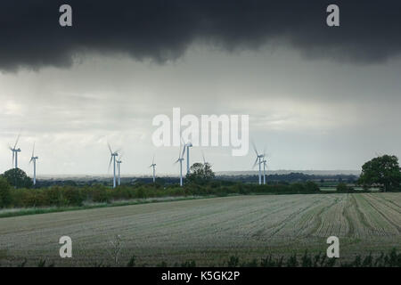 Henlow, Bedfordshire, Wind turbines with heavy dark grey weather in the background. View across a farmers field. Stock Photo