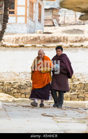 Villager assists senior monk outside the Buddhist temple in Ura, (Ura Mang Gi Lakhang) Central Bhutan. Stock Photo