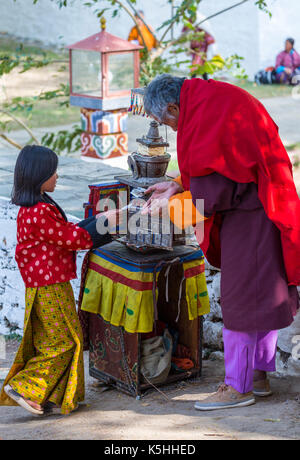 Young girl making a donation to a monk outside Punakha Dzong, Western Bhutan, during the annual Drubchen and Tsechu. Stock Photo