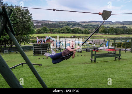 Girl having fun swinging on zip wire in adventure play park in Denny, Scotland Stock Photo