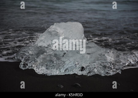 Chunk of clear gleaming glacier ice washed up on black sand beach Stock Photo