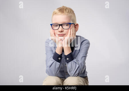 Portrait of caucasian blond boy in glasses looking with bored facial expression to camera on white background. Stock Photo