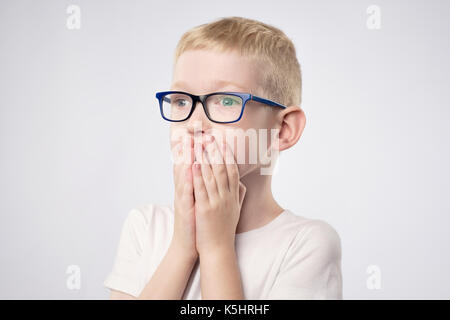 Scared litle kid boy with blond hair holding hands on face because he is afraid Stock Photo