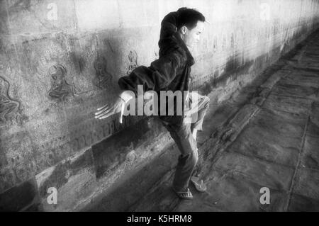 Guide demonstrates Apsara dancing in columnaded walkway of Angkor Wat temple, Cambodia. Note Apsara dancers incised on wall behind him. October 30, 1996. Image originated on B/W infrared film. Epson Expression 10000XL Stock Photo