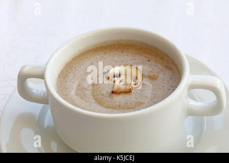 Portion of champignon mushroom cream soup in white porcelain tureen pot on the table, close up, high key, high angle view Stock Photo