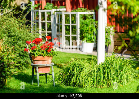 Hollowed wooden chair outdoors with flowerpot inside. Garden and flagpole in background Stock Photo