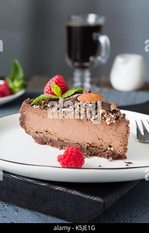 Slice of chocolate cheesecake decorated with nuts, raspberries and mint leaf. Closeup view, vertical composition Stock Photo