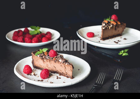 Two pieces of chocolate cheesecake decorated with raspberries and mint on dark background. Horizontal composition Stock Photo