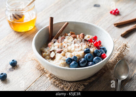 Oatmeal porridge with blueberries, almonds, cinnamon, honey, linseeds and red currants in bowl. Super food for healthy nutritious breakfast Stock Photo