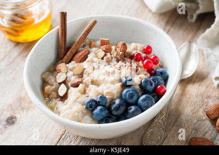 Oatmeal porridge with blueberries, almonds, cinnamon, honey, linseed and red currants in bowl. Healthy breakfast food Stock Photo
