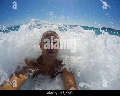 Fit middle-aged man standing in the ocean. Man having fun in large sea waves. Man hit by wave at sea. Stock Photo