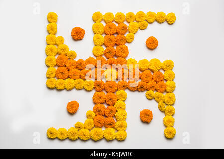 stock photo of hindu auspicious symbol called Swastika made using marigold flower or zendu or genda phool, Flower rangoli in the shape of Swastika for Stock Photo