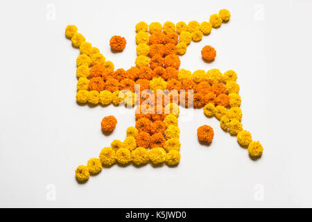 stock photo of hindu auspicious symbol called Swastika made using marigold flower or zendu or genda phool, Flower rangoli in the shape of Swastika for Stock Photo