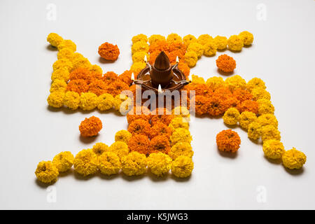 stock photo of hindu auspicious symbol called Swastika or swastik made using marigold flower/zendu/genda phool & diwali diya / clay lamp, Flower rango Stock Photo