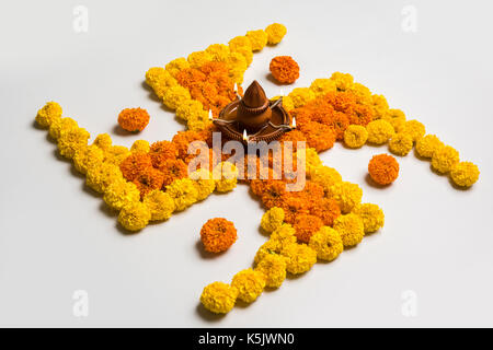 stock photo of hindu auspicious symbol called Swastika or swastik made using marigold flower/zendu/genda phool & diwali diya / clay lamp, Flower rango Stock Photo