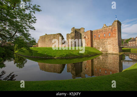 Stunning view of 13th century Rothesay castle with high stone walls reflected in mirror surface of water in moat under blue sky, Isle of Bute Scotland Stock Photo