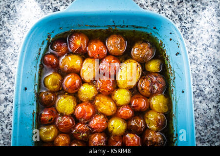 Roasted cherry tomatoes in a blue baking dish.  The cherry tomatoes are roasted with extra virgin olive oil, balsamic vinegar, and a touch of brown Su Stock Photo