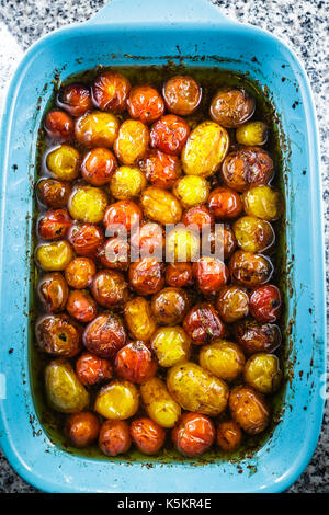 Roasted cherry tomatoes in a blue baking dish.  The cherry tomatoes are roasted with extra virgin olive oil, balsamic vinegar, and a touch of brown Su Stock Photo