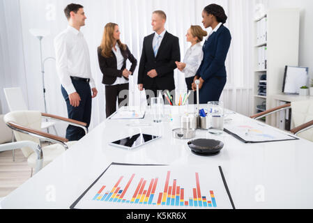 Happy Businesspeople Having Conversation With Digital Tablet And Graph On Desk Stock Photo